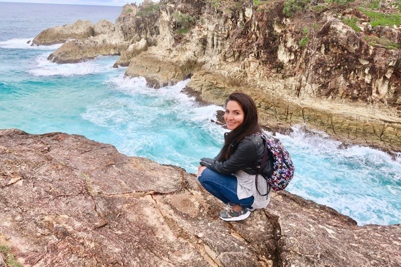 Excursiones Australia estudiante morena con mochila y arrodillada en una roca en la isla Stradbroke de Australia